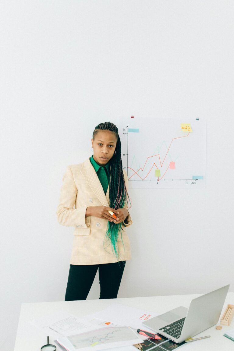 Businesswoman analyzing charts in an office setting with a laptop and diagrams.